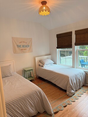 A bedroom with two beds, a small table, a wall sign, and a window with blinds. - Knights by the Sea l New Coastal 2-bedroom home l Walk to Long Sands Beach (York)