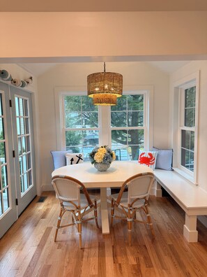 A dining area with a round table, wicker chairs, a woven pendant light, and a bench with cushions. - Knights by the Sea l New Coastal 2-bedroom home l Walk to Long Sands Beach (York)