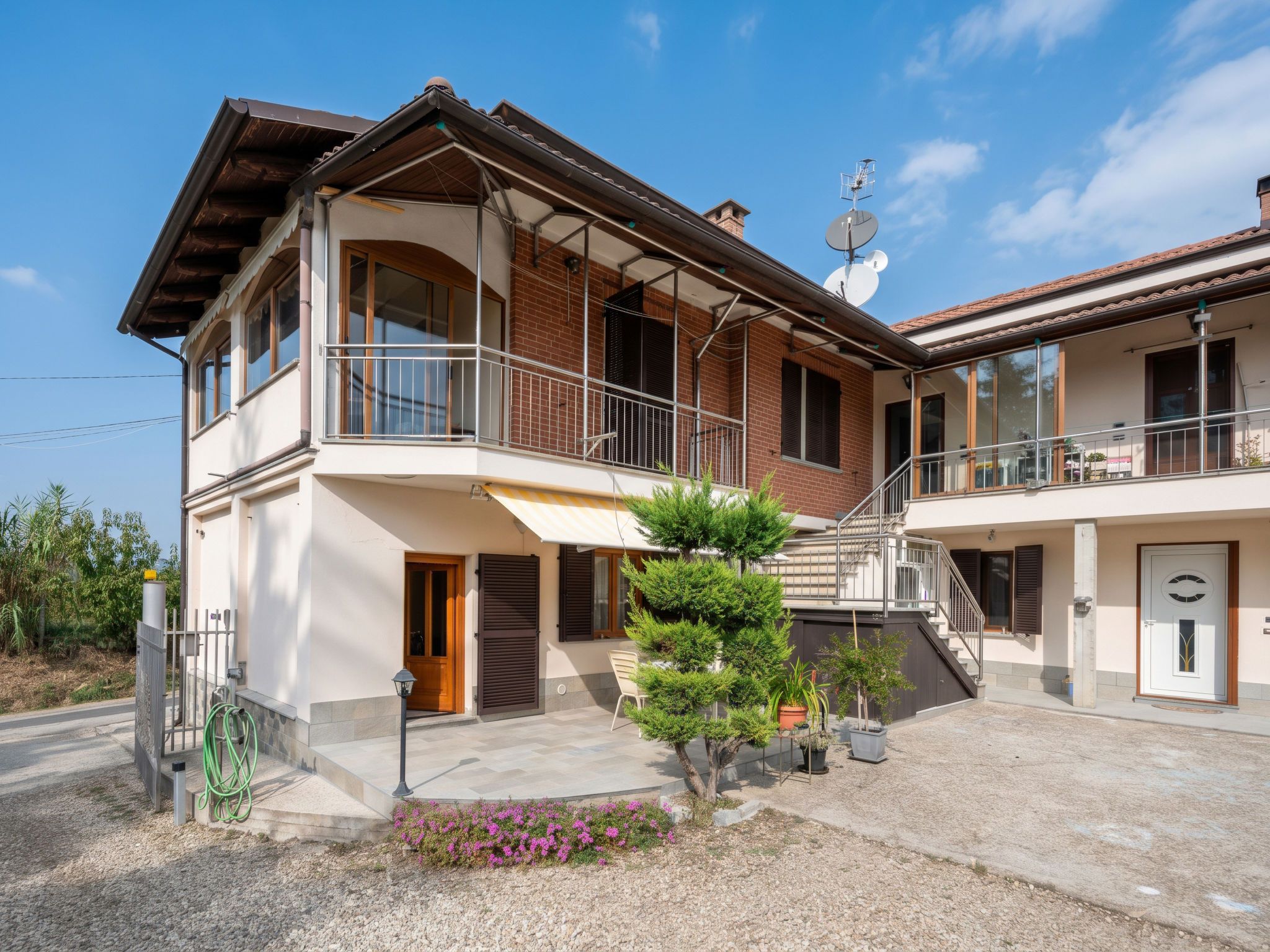 A two-story house with a balcony, a satellite dish, and a small garden with flowers.