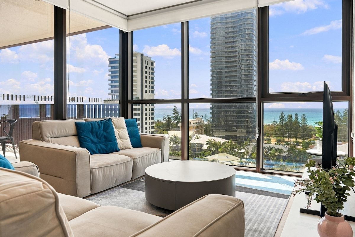 A modern hotel room with a large window, a sofa, a round coffee table, and a potted plant.