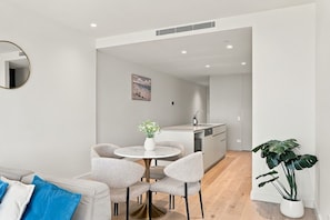 A modern living room with a round table, grey chairs, a white sofa, and a potted plant. - Water Views, Heated Pool & Parking (Mermaid Beach)