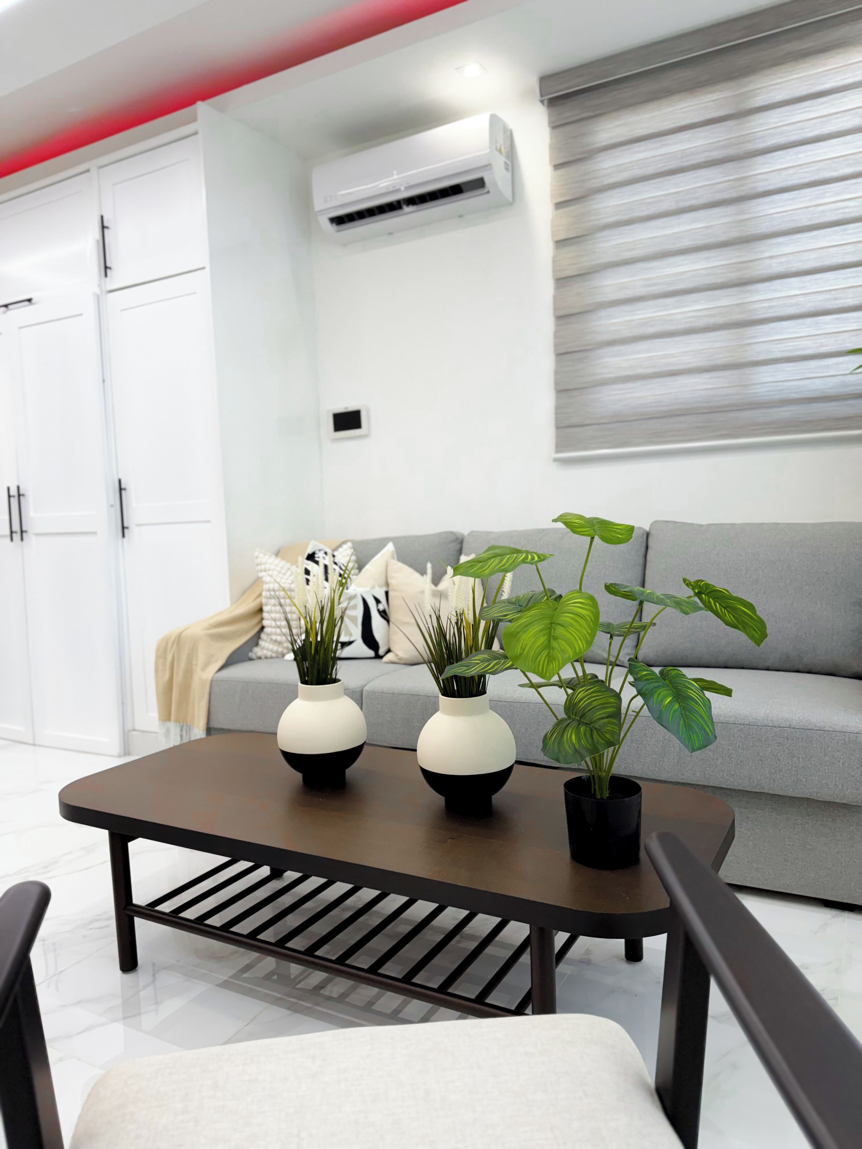 Uma sala de estar moderna com um sofá cinza, uma mesa de centro com vasos e uma planta em vaso.