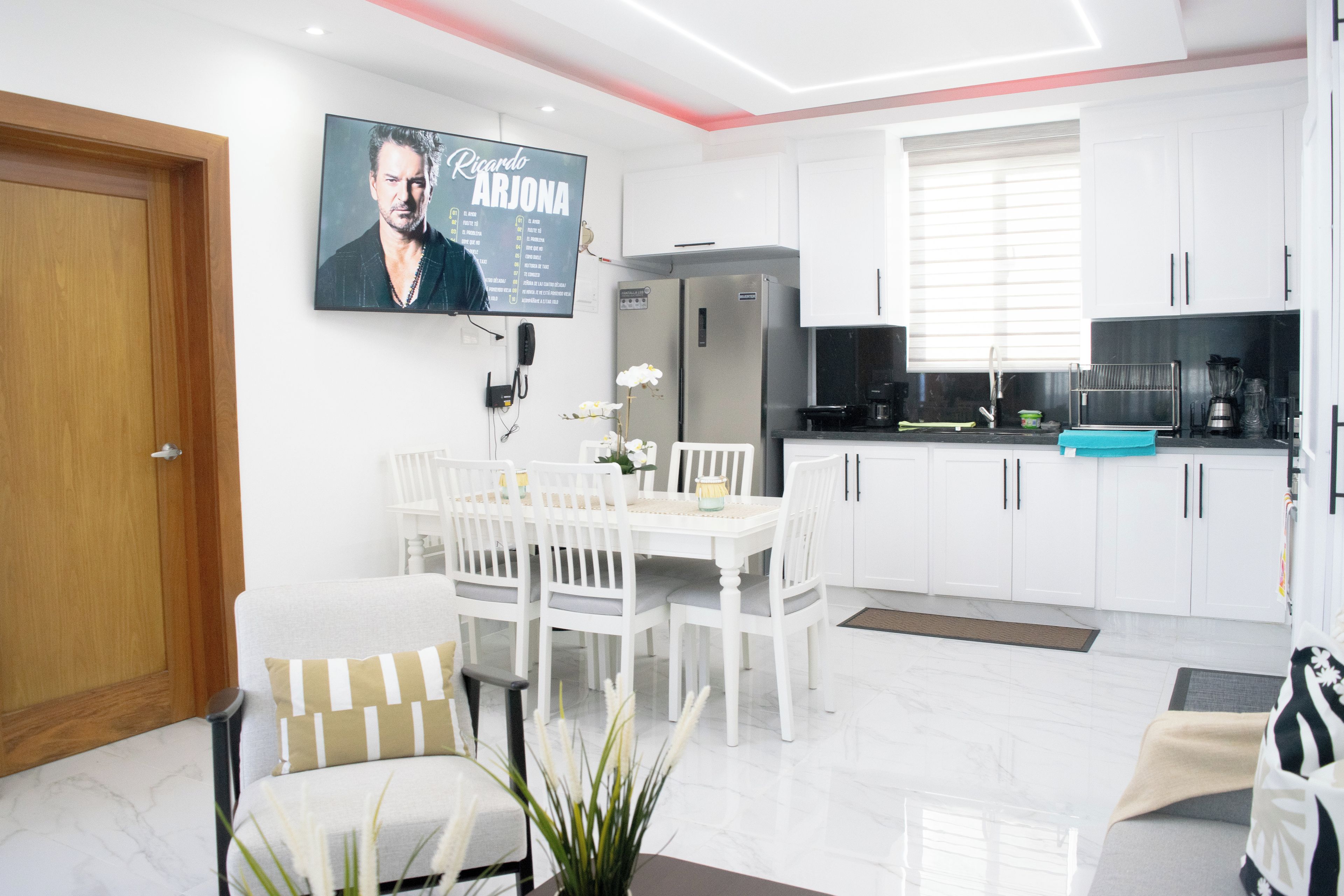 Uma cozinha moderna com armários brancos, geladeira e um espaço de refeições com mesa e cadeiras.