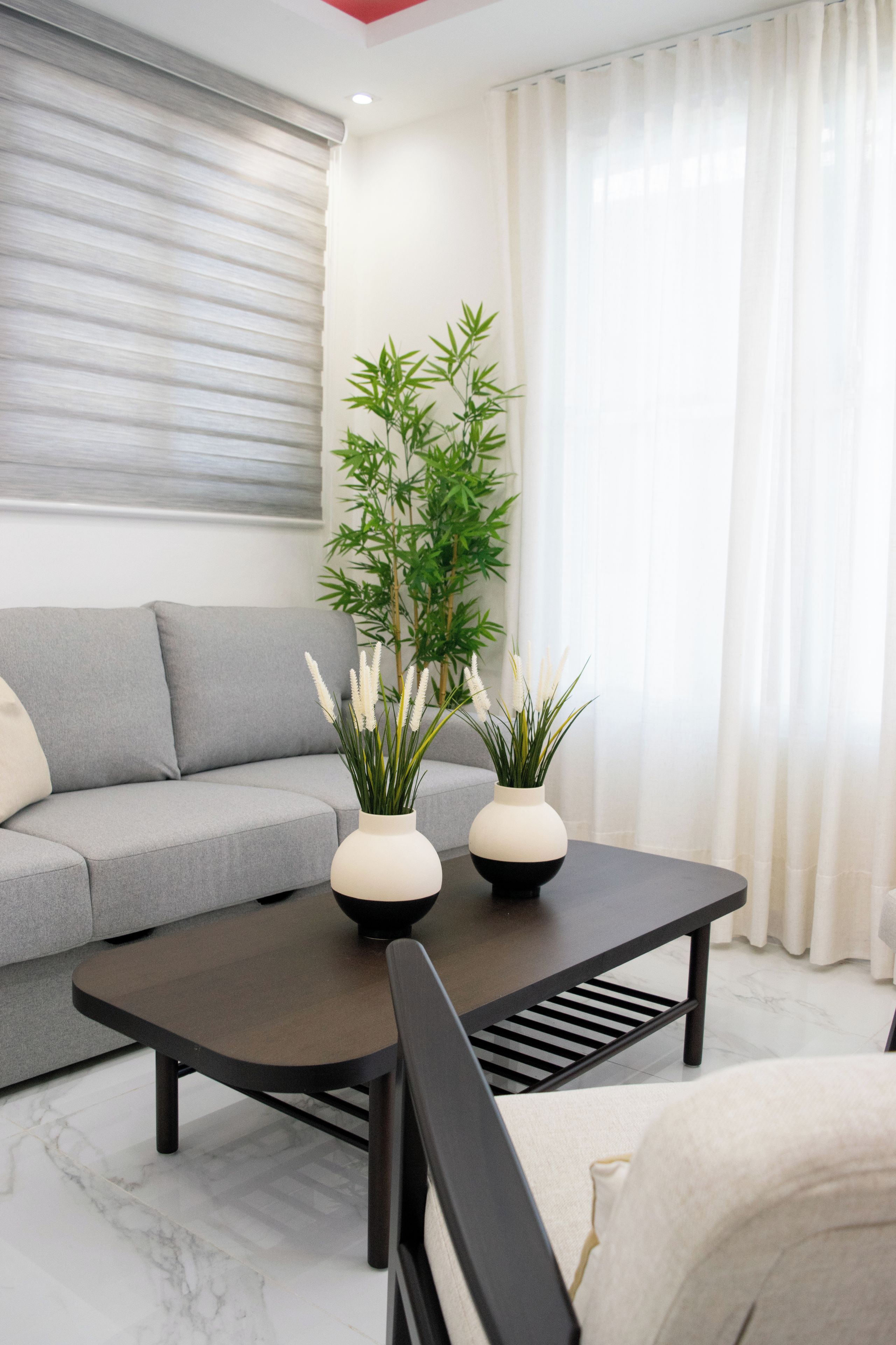 Uma sala de estar moderna com um sofá cinza, uma mesa de centro com dois vasos preto e branco, e uma planta de bambu.