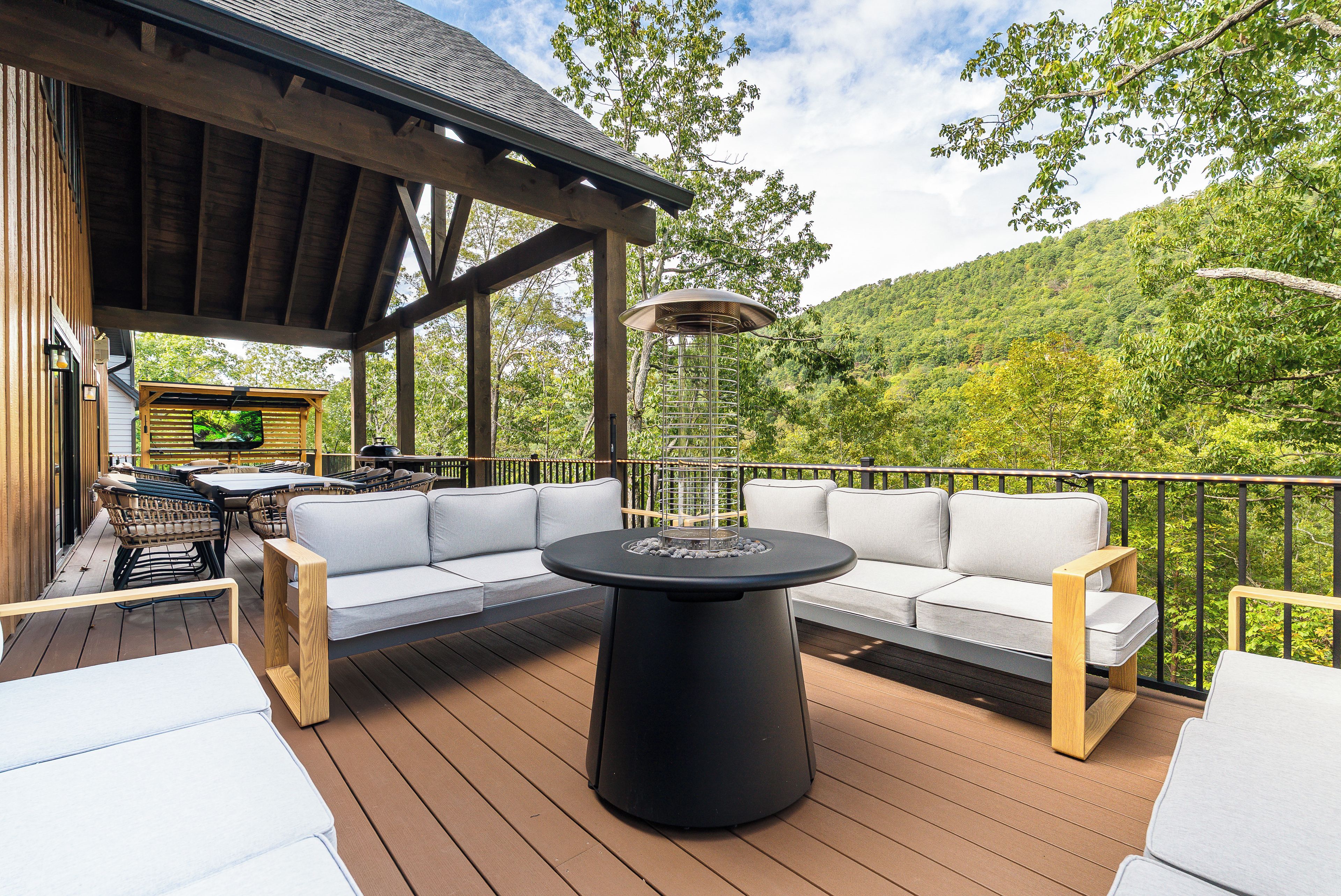 A deck with a sofa and a round table, overlooking a forested hillside.