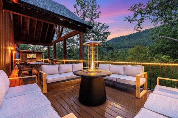 An outdoor deck with a fire feature, seating, and a view of the surrounding landscape.