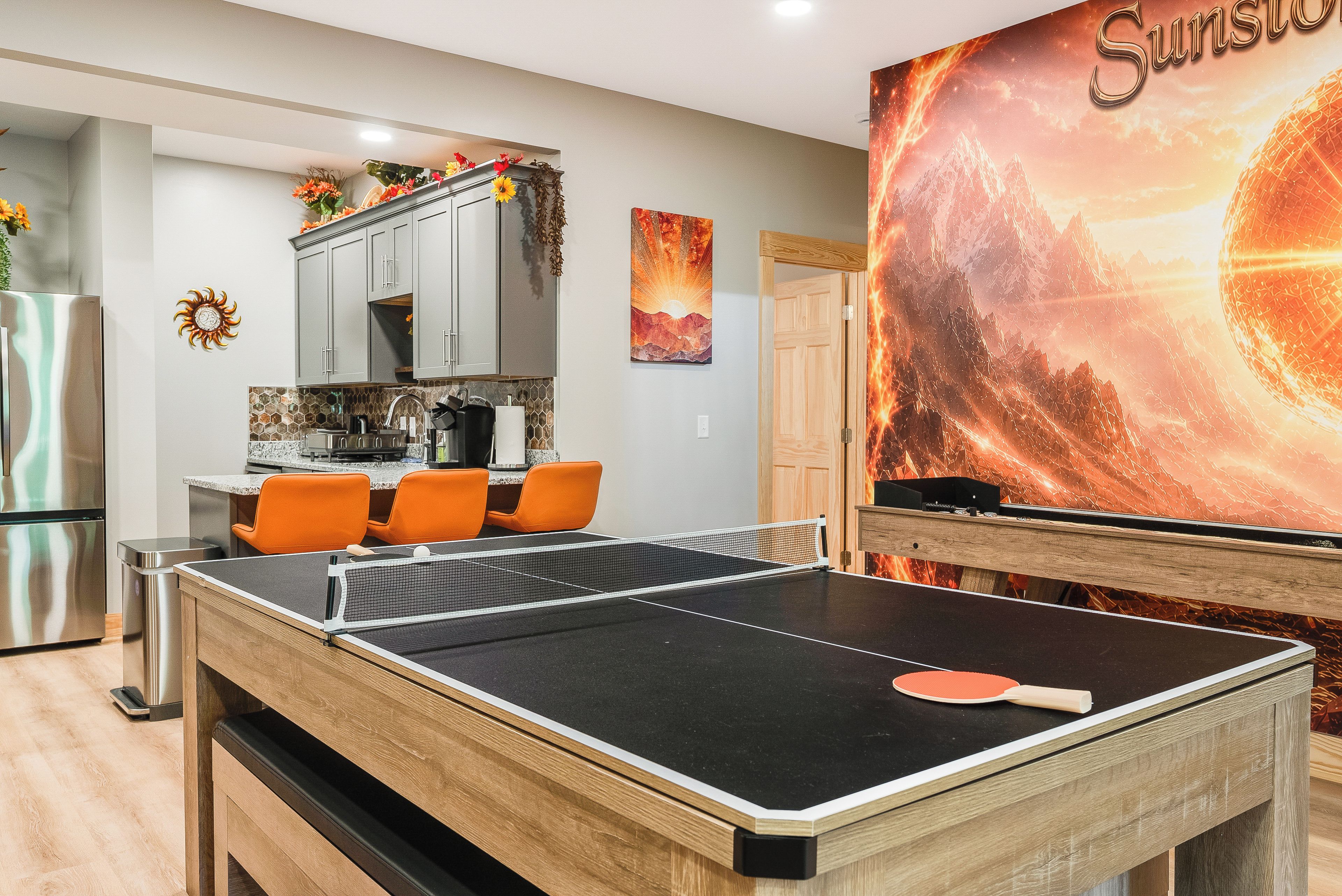 A room with a ping pong table, a kitchen area, and a large wall mural.
