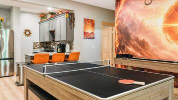 A room with a ping pong table, a kitchen area, and a large wall mural.