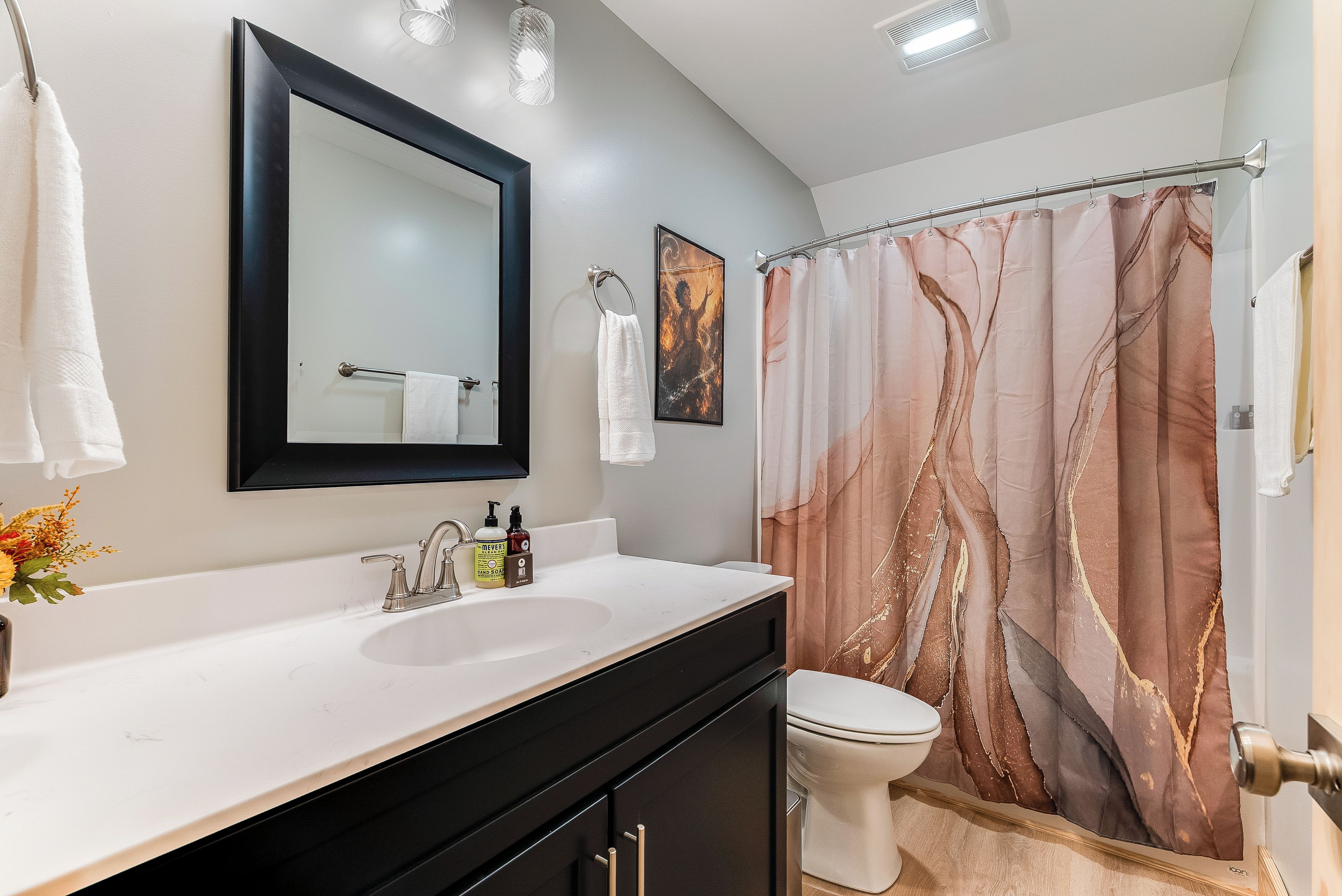 A bathroom with a white sink, black cabinets, a toilet, a shower curtain with a tree design, and a mirror above the sink.