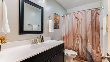 A bathroom with a white sink, black cabinets, a toilet, a shower curtain with a tree design, and a mirror above the sink.