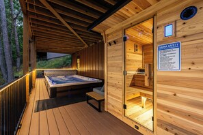 A wooden sauna with a hot tub, a safety sign, and a view of the surrounding forest.