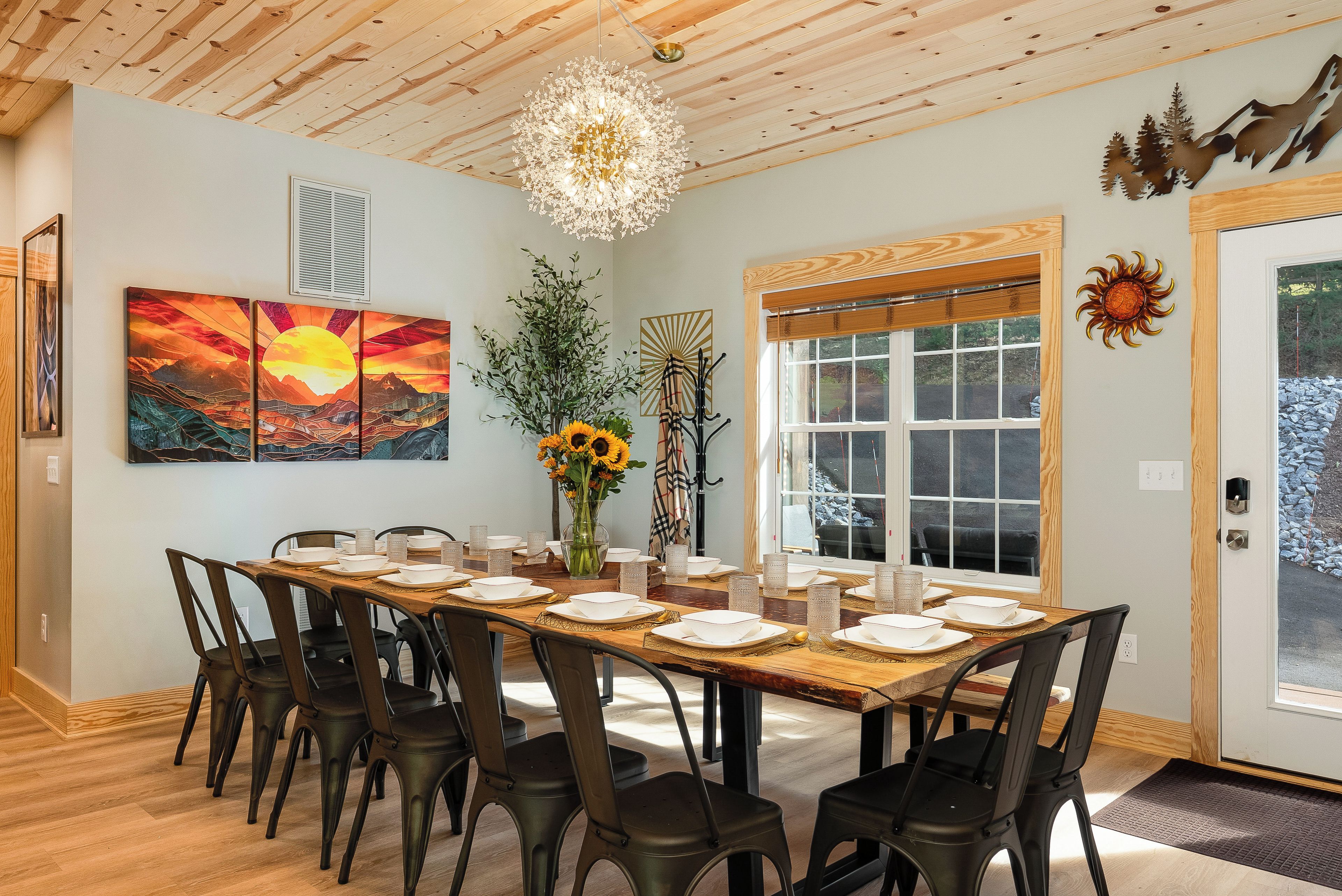 A dining area with a wooden table set for six, surrounded by chairs, a chandelier, and artwork on the walls.