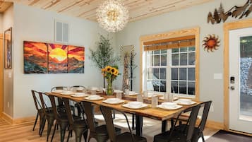 A dining area with a wooden table set for six, surrounded by chairs, a chandelier, and artwork on the walls.