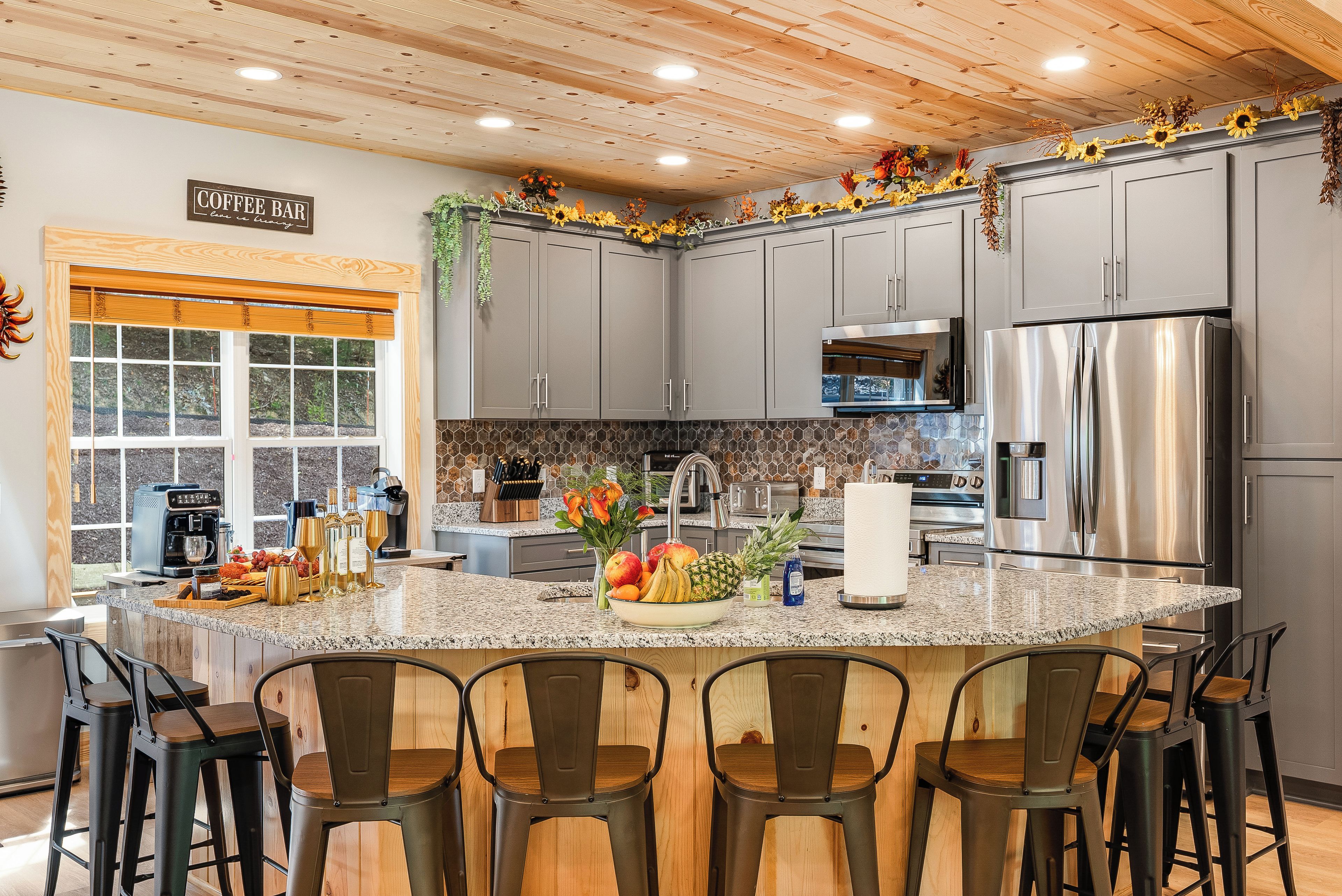 A modern kitchen with grey cabinets, a stainless steel refrigerator, and a breakfast bar with chairs.