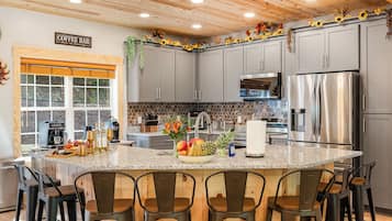 A modern kitchen with grey cabinets, a stainless steel refrigerator, and a breakfast bar with chairs.