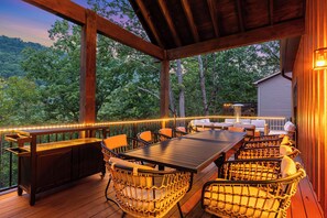 Una terraza al aire libre con una mesa y sillas de madera, rodeada por una barandilla con luces de cuerda.