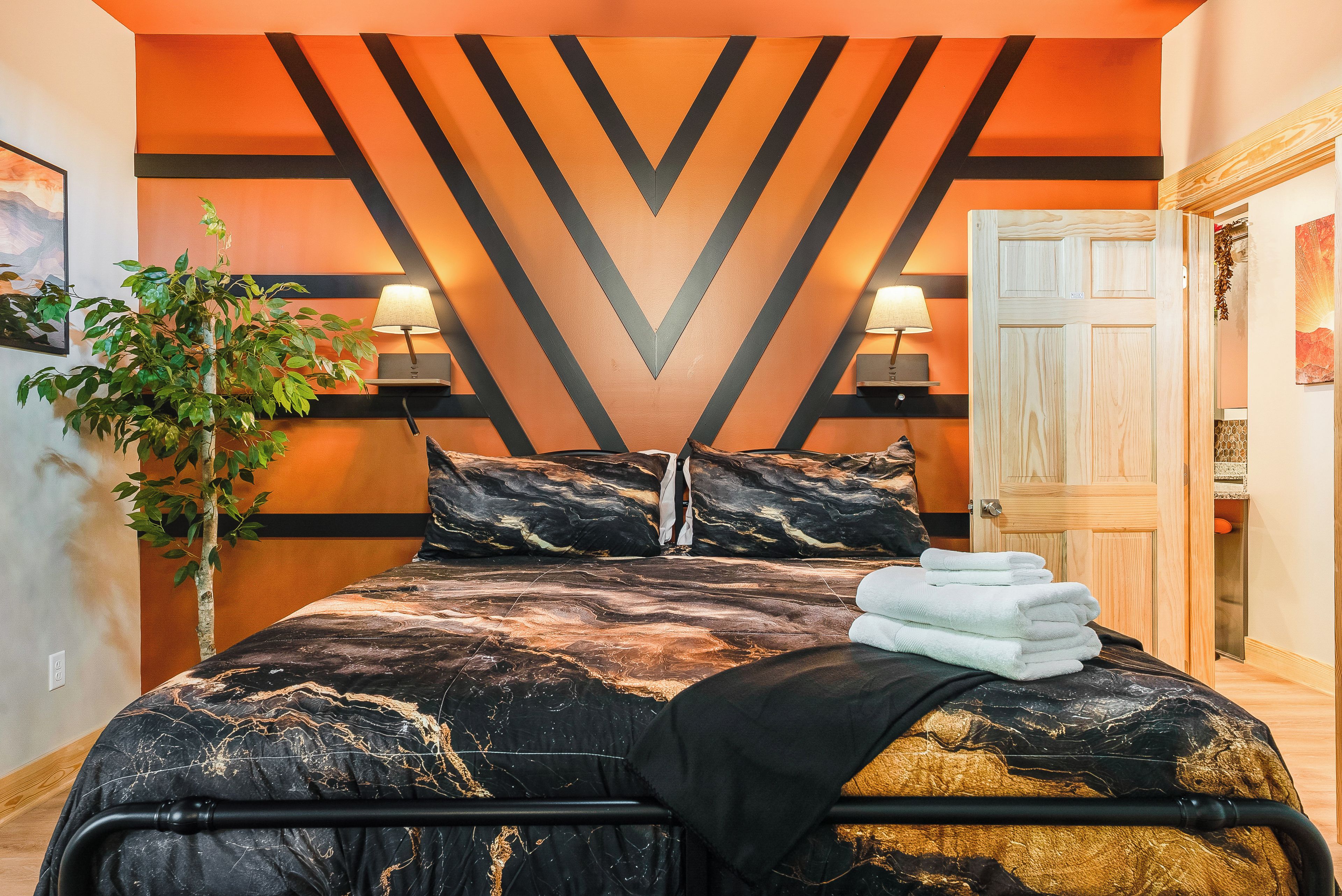 Ein modernes Schlafzimmer mit einem Bett, zwei Nachttischlampen, einem Blumentopf und einer Tür.