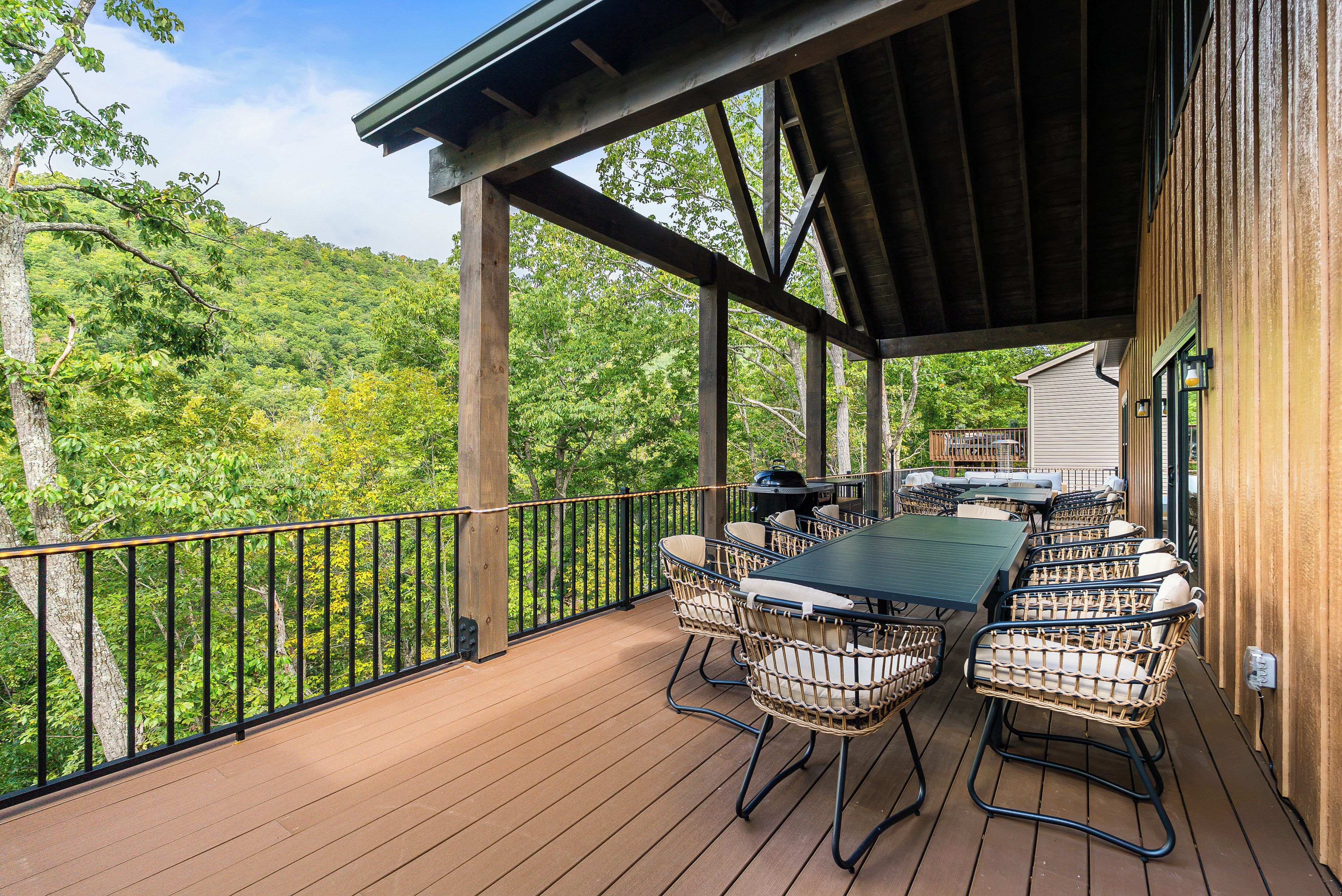 A covered outdoor deck with a table and chairs, surrounded by a wooden railing.