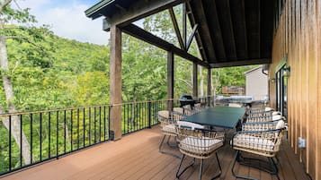 A covered outdoor deck with a table and chairs, surrounded by a wooden railing.