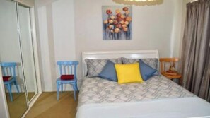 A bedroom with a bed, a chair, a painting, and a window. - Sapphire Sands at Pambula Beach (Pambula Beach)
