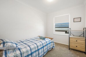 Un dormitorio con una cama, un aparador de madera, una ventana con persianas y un certificado enmarcado en la pared.
