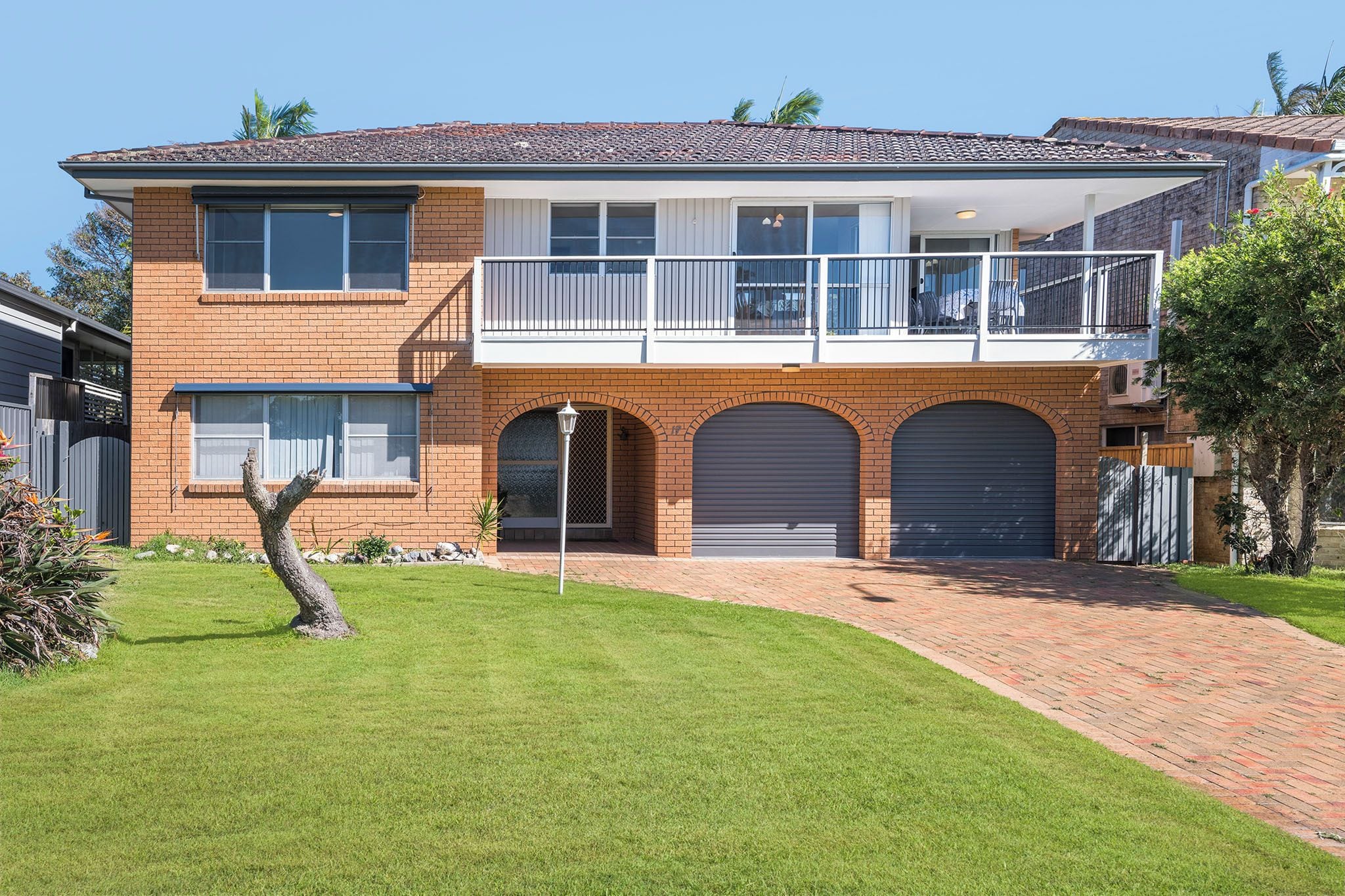 A two-story house with a balcony, garage doors, and a well-maintained lawn.