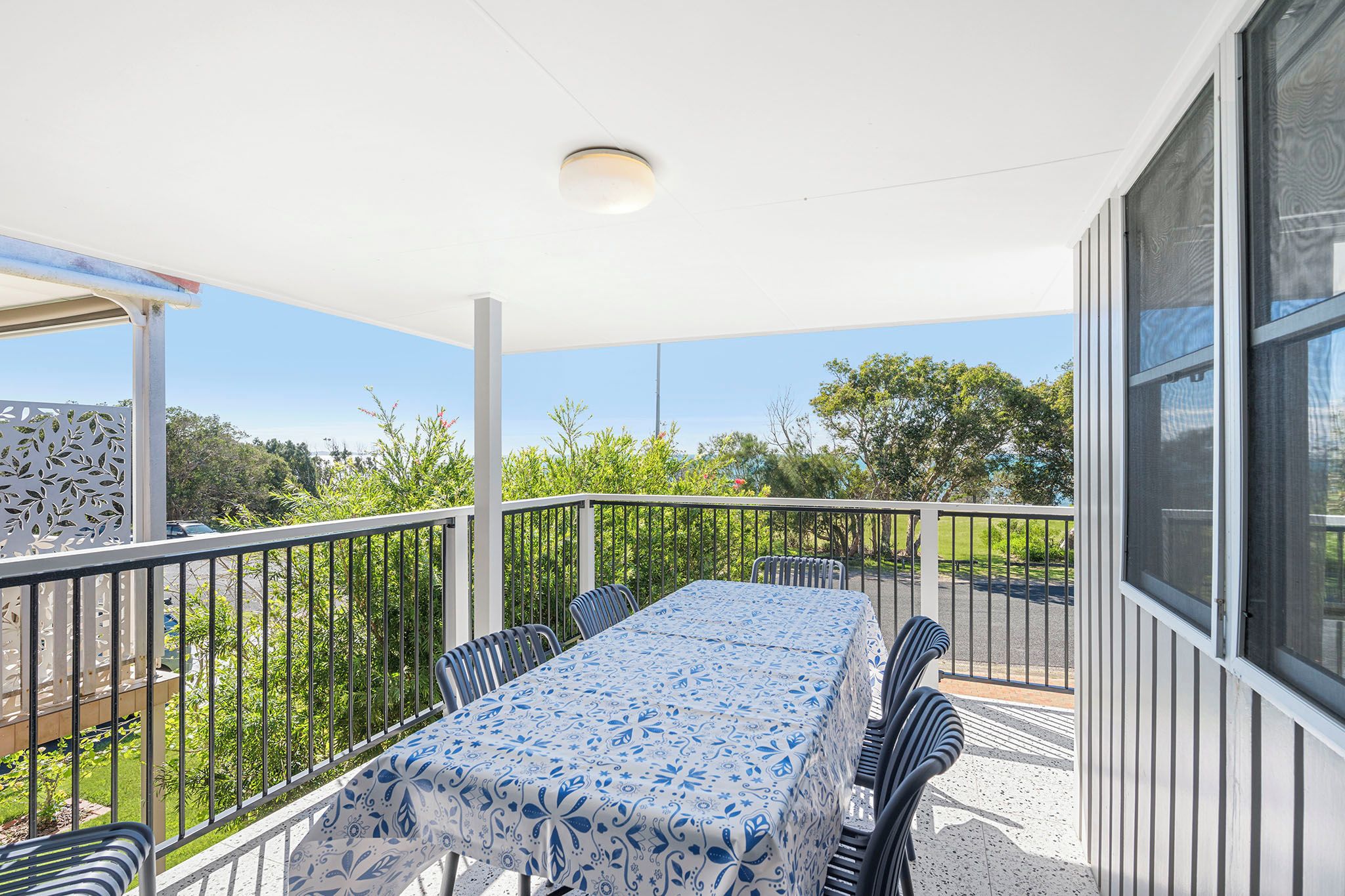 Un patio techado al aire libre con una mesa y sillas, rodeado por una barandilla, con vistas a un paisaje verde.