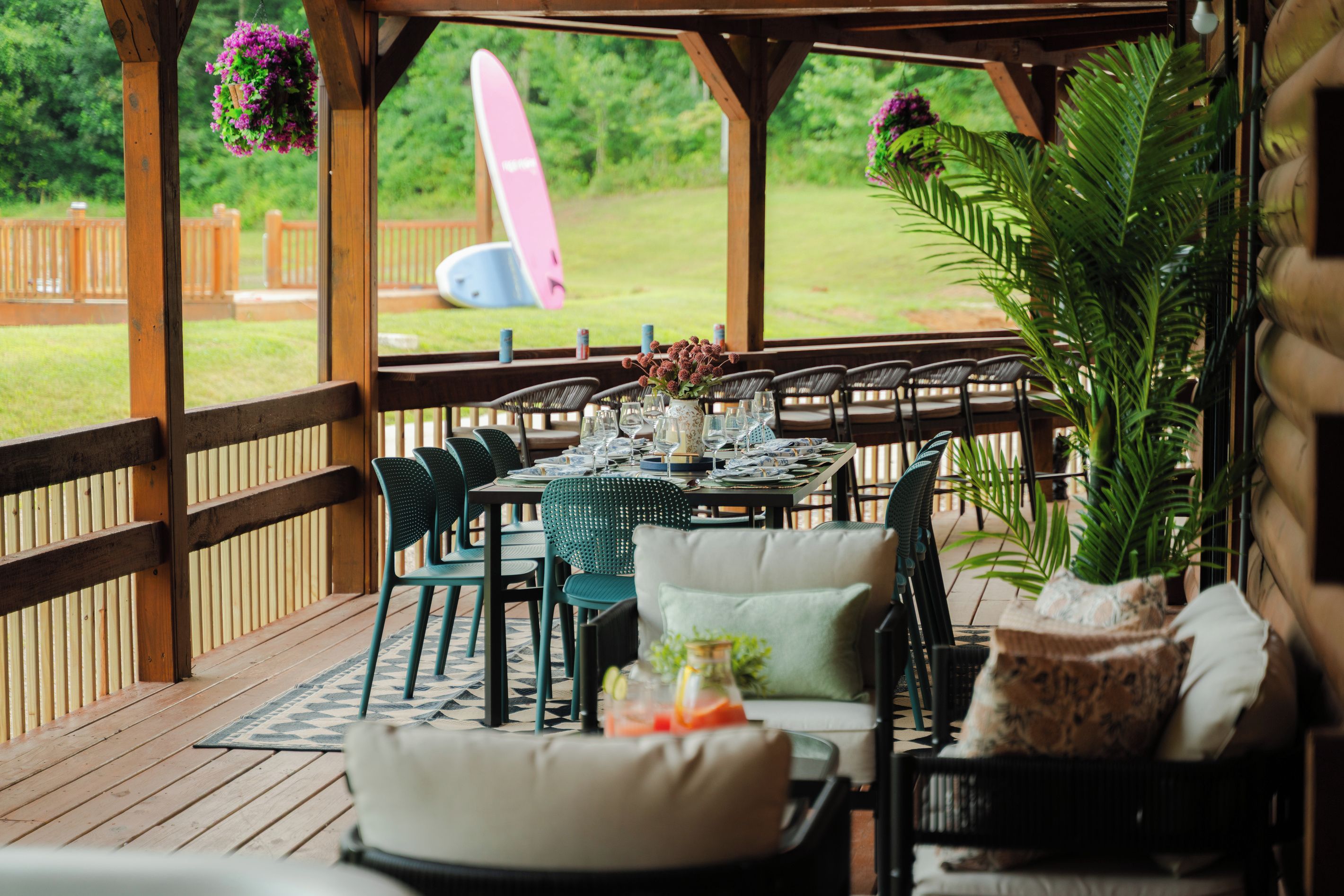 Une terrasse extérieure avec une plateforme en bois, des chaises vertes, une table dressée pour le repas et une vue sur un jardin.