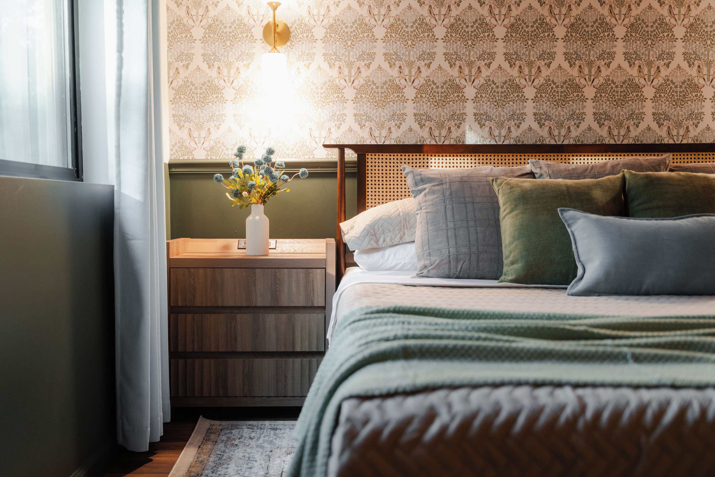 Una camera da letto con un letto, un comodino, una lampada e una finestra con tende.