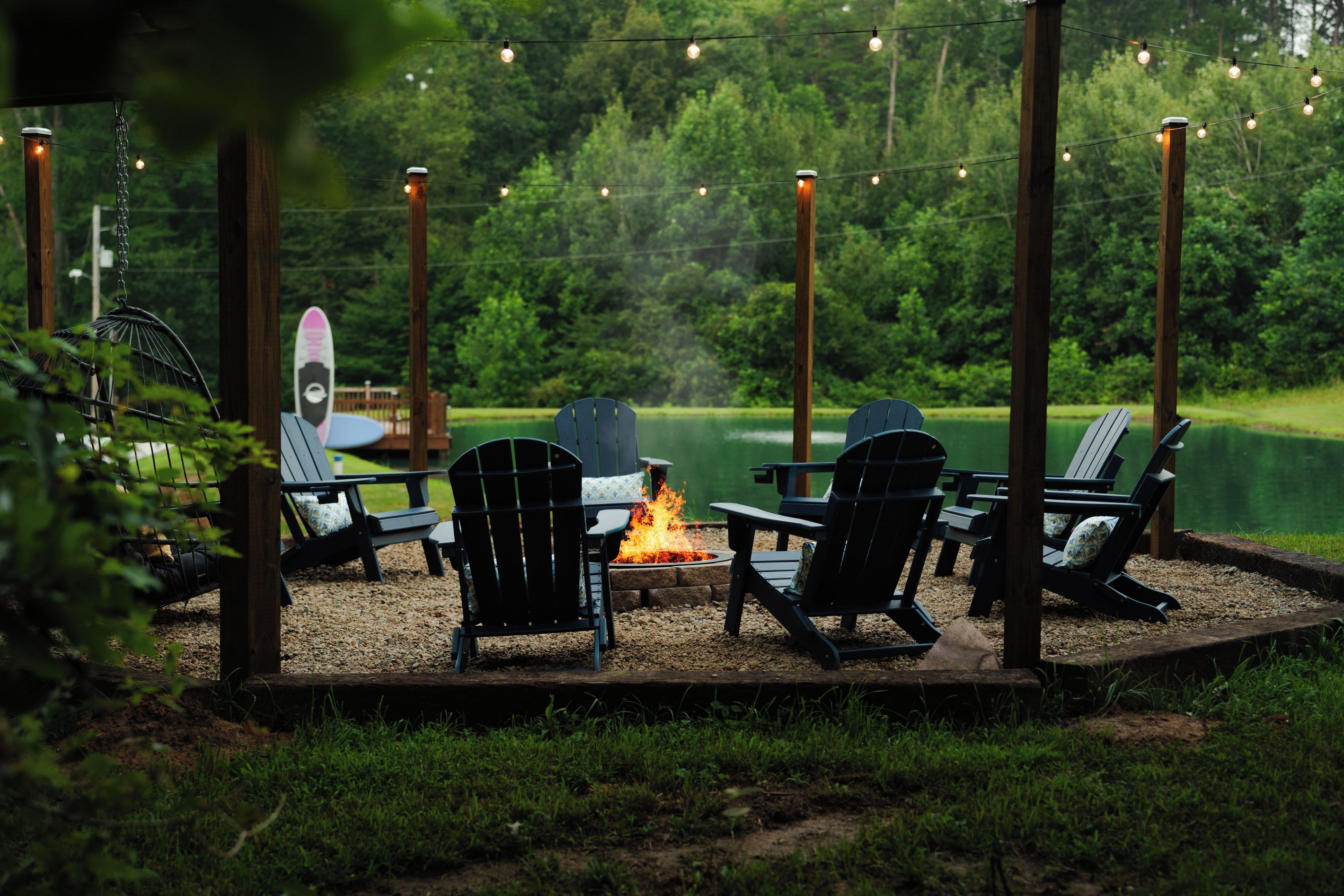 An outdoor seating area with chairs and a fire pit, surrounded by a wooden deck and string lights.