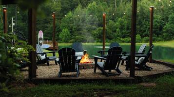 An outdoor seating area with chairs and a fire pit, surrounded by a wooden deck and string lights.