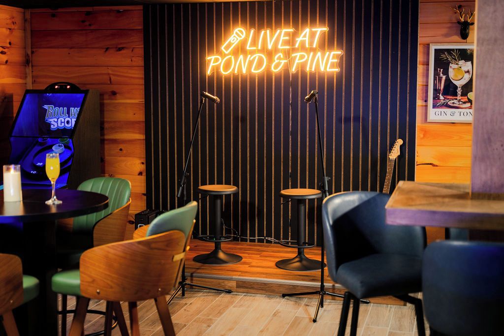 Un coin bar accueillant, avec un panneau néon indiquant « MUSIQUE EN DIRECT AU POND & PINE », un juke-box et des tabourets de bar.