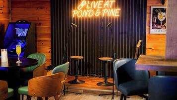 Un coin bar accueillant, avec un panneau néon indiquant « MUSIQUE EN DIRECT AU POND & PINE », un juke-box et des tabourets de bar.