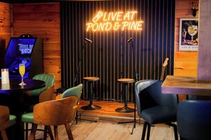 Eine gemütliche Bar mit einer Neonreklame mit der Aufschrift 'LIVE AT POND & PINE', einer Jukebox und Barhocker.