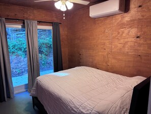 Quarto com cama, ventilador de teto, ar condicionado e janela com cortinas.