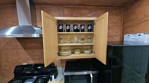 A kitchen with a wooden cabinet containing bottles, glasses, and plates. - Base Camp on Cherry Hill — Fife Lake, MI 

Cabin, Sleeps 4–8 (Fife Lake)