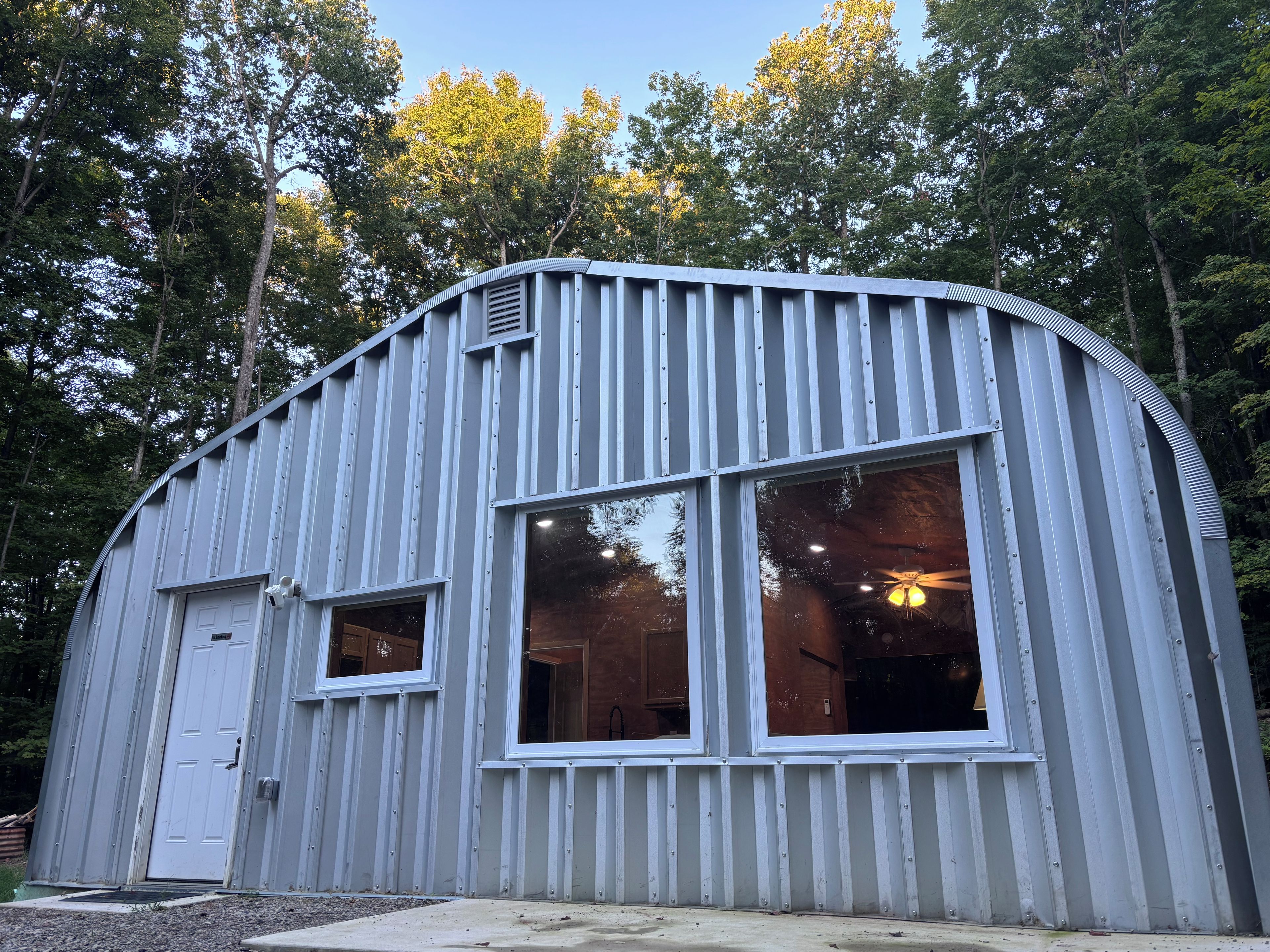 A metal building with large windows and a door, surrounded by trees.