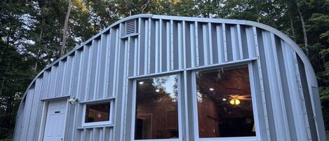 A metal building with large windows and a door, surrounded by trees.