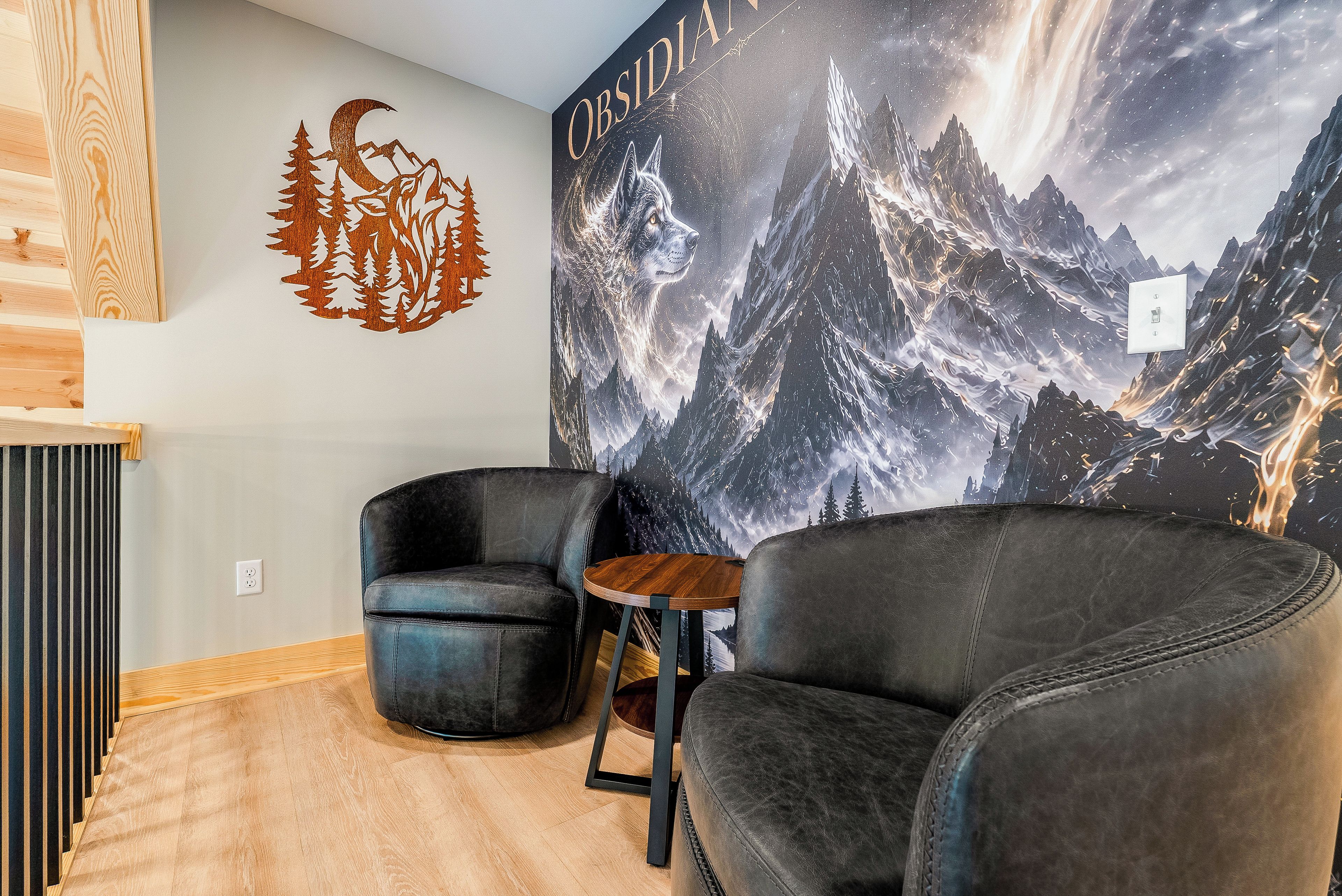 Una habitación con dos sillones de cuero, una pequeña mesa de madera y un mural en la pared que representa un paisaje montañoso.
