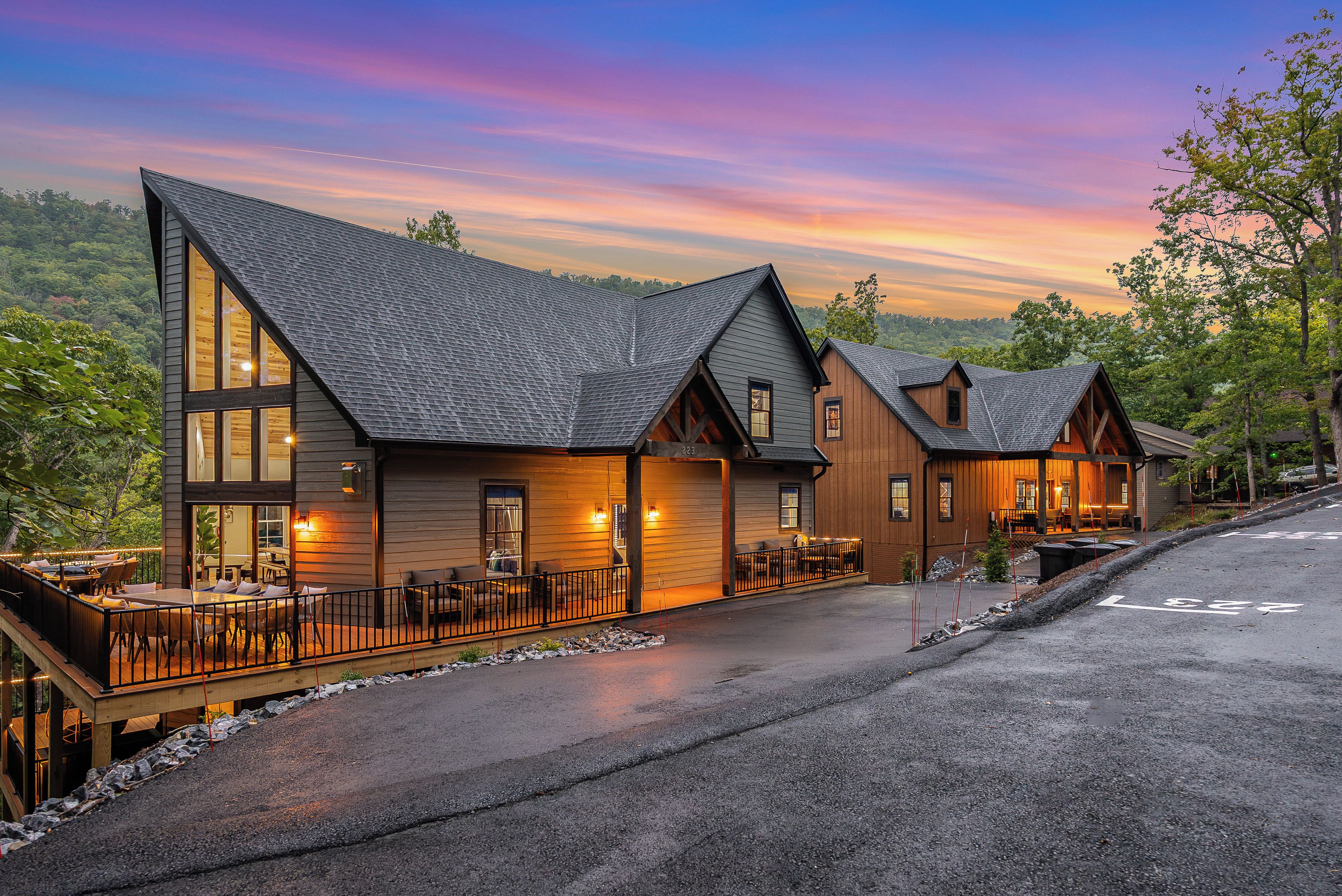 A modern lodge with large windows, a covered outdoor seating area, and a view of the surrounding forest.