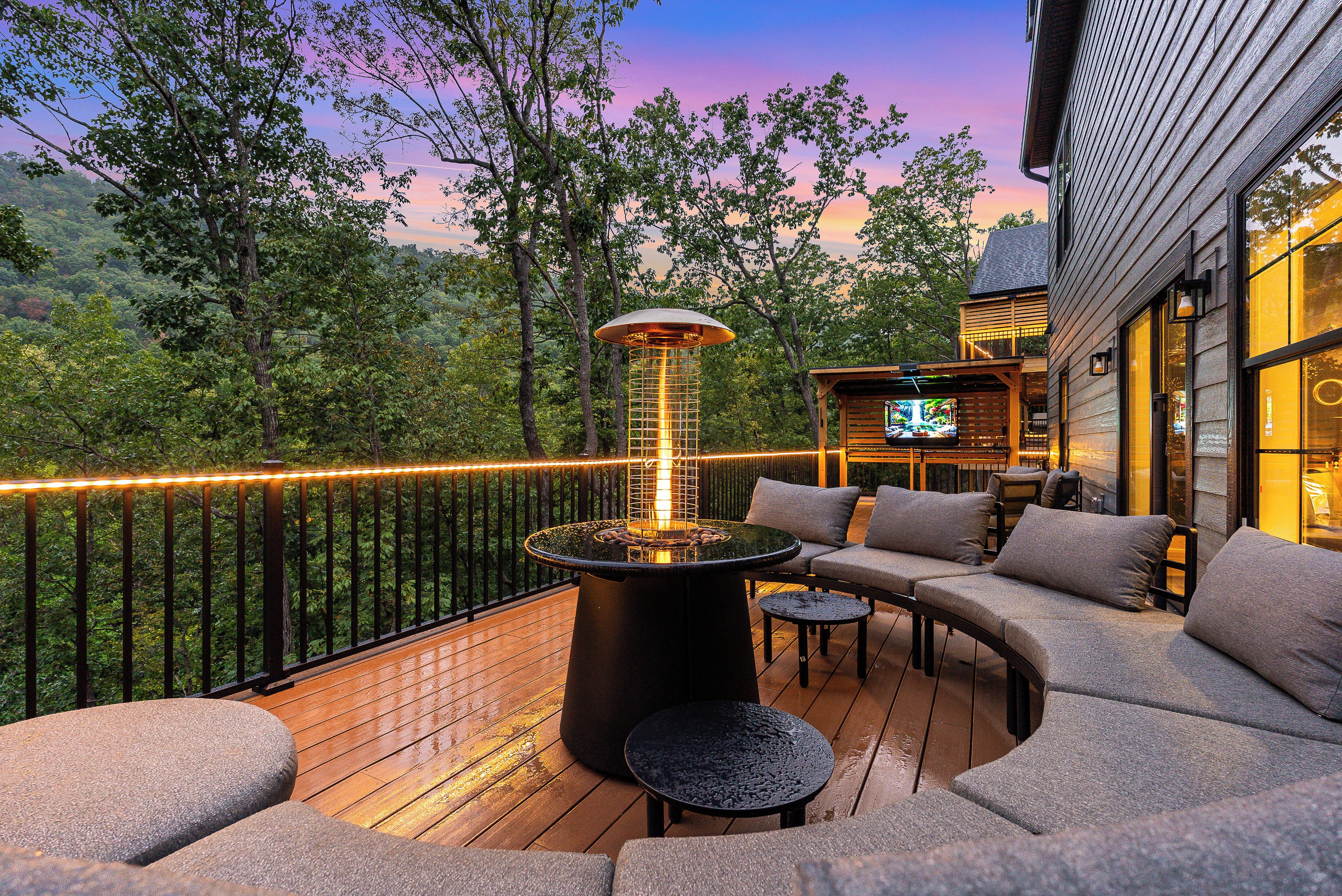 An outdoor deck with a heated outdoor seating area, a fire feature, and a view of the surrounding forest.