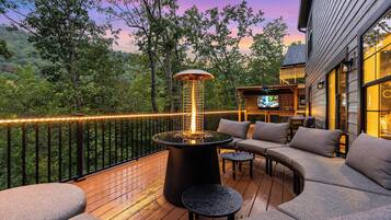An outdoor deck with a heated outdoor seating area, a fire feature, and a view of the surrounding forest.