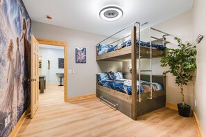 Una cama individual con estructura de madera y ropa de cama azul, una planta en maceta y una pared con un mural de temática celestial.