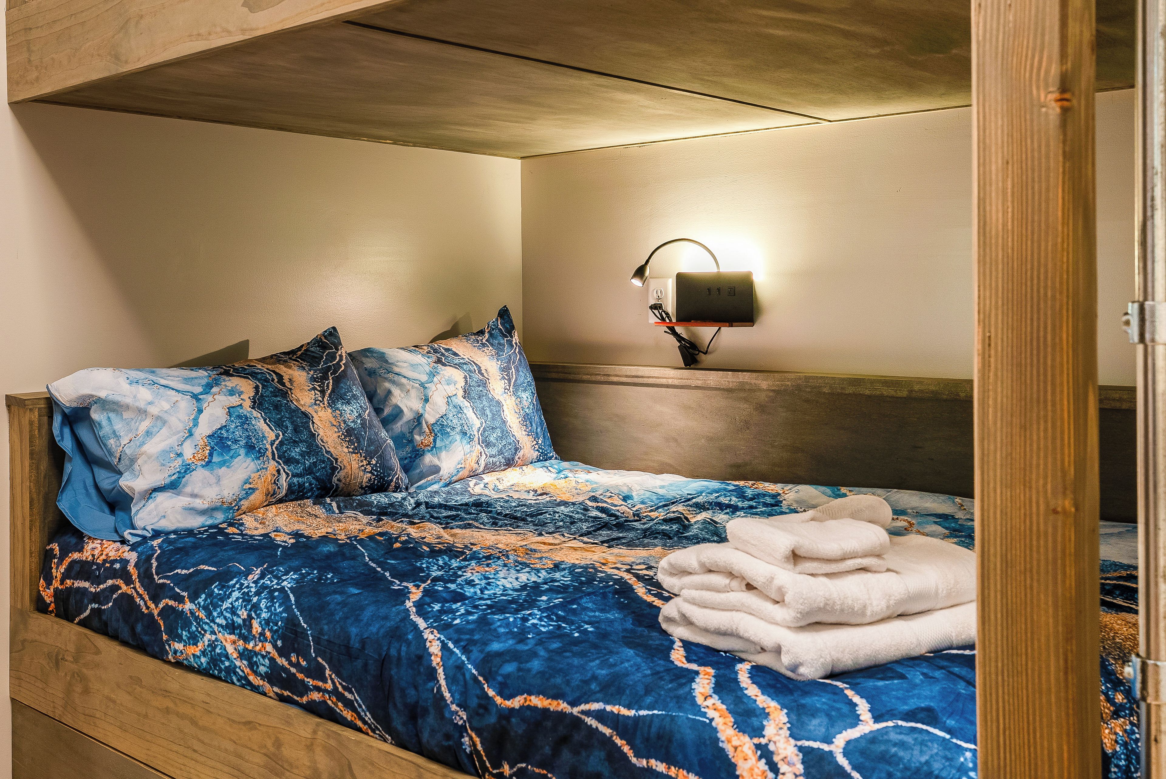 A hotel room with a bed, pillows, a blanket, a wall-mounted lamp, and a wooden headboard.