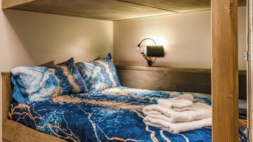 A hotel room with a bed, pillows, a blanket, a wall-mounted lamp, and a wooden headboard.