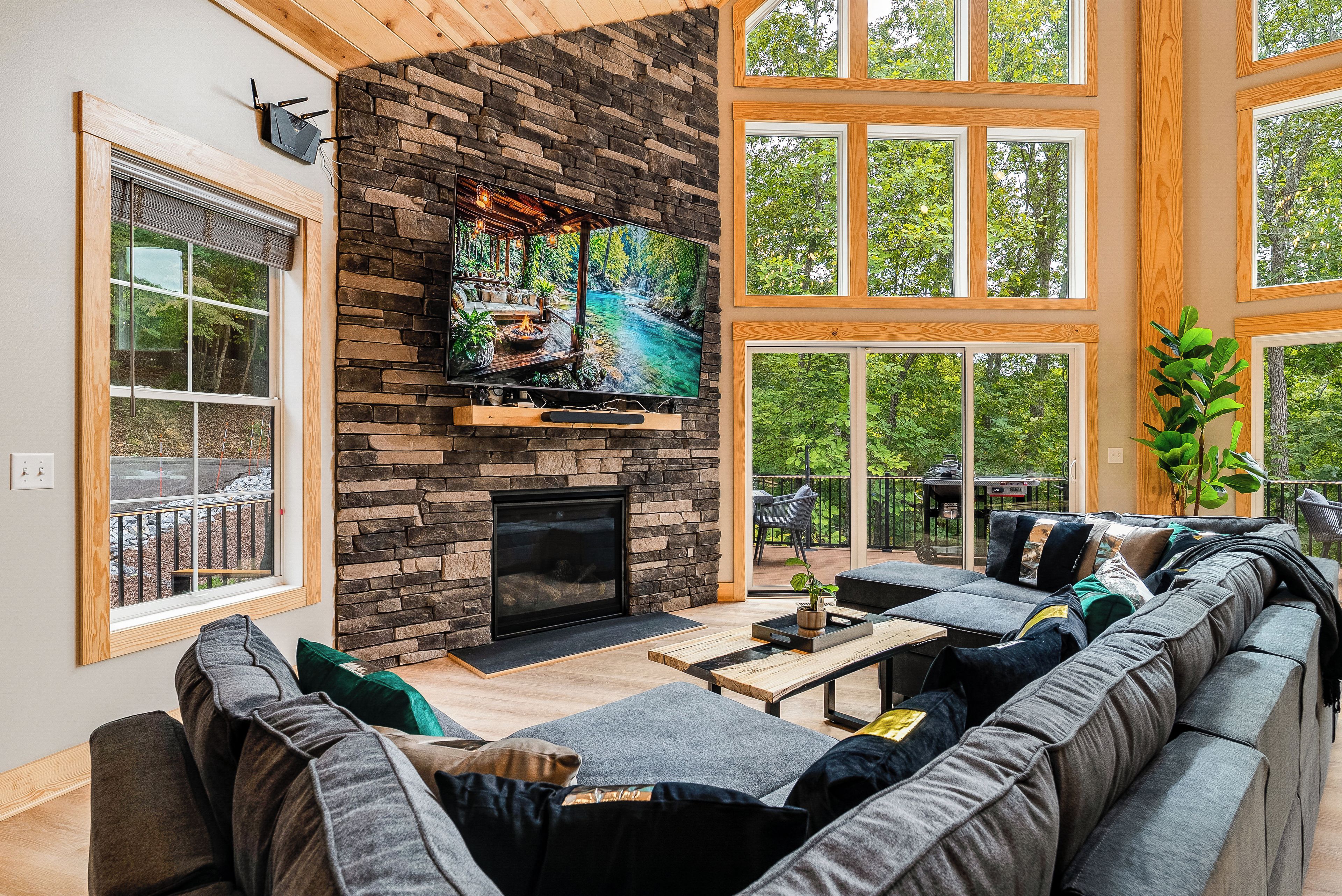 A modern living room with a stone fireplace, large windows, and a comfortable seating area.