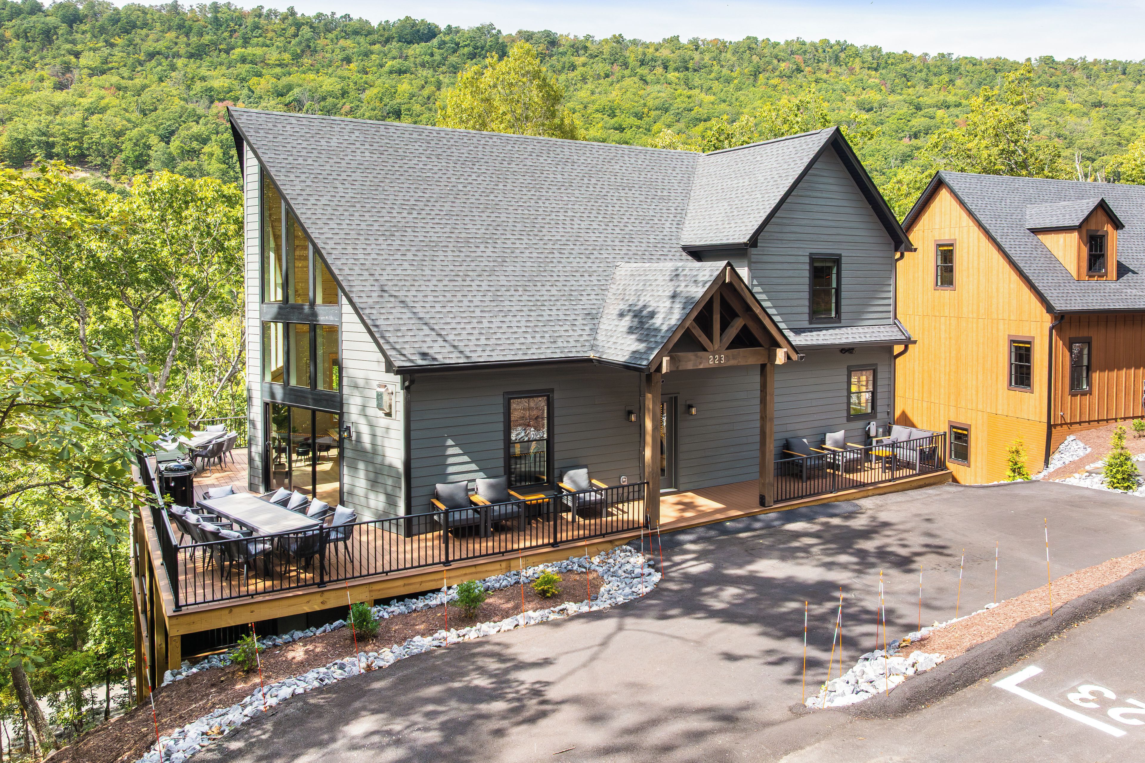 A two-story building with a covered patio area, a stone pathway, and a view of a forested hillside.