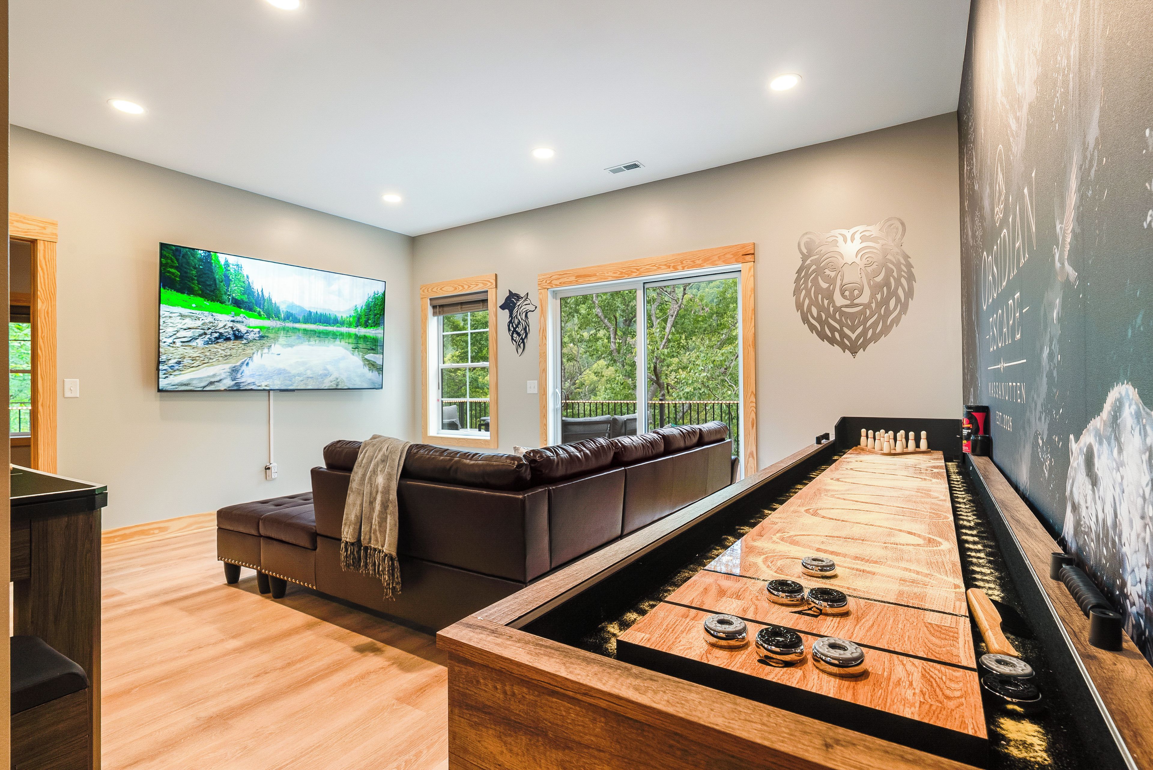 A room with a pool table, a large flat-screen TV, a sofa, and a bear mural.