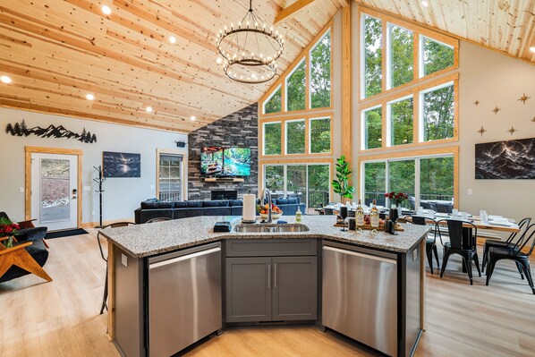 A modern kitchen with a large island, a stone fireplace, and a dining area with a view of the outdoors.