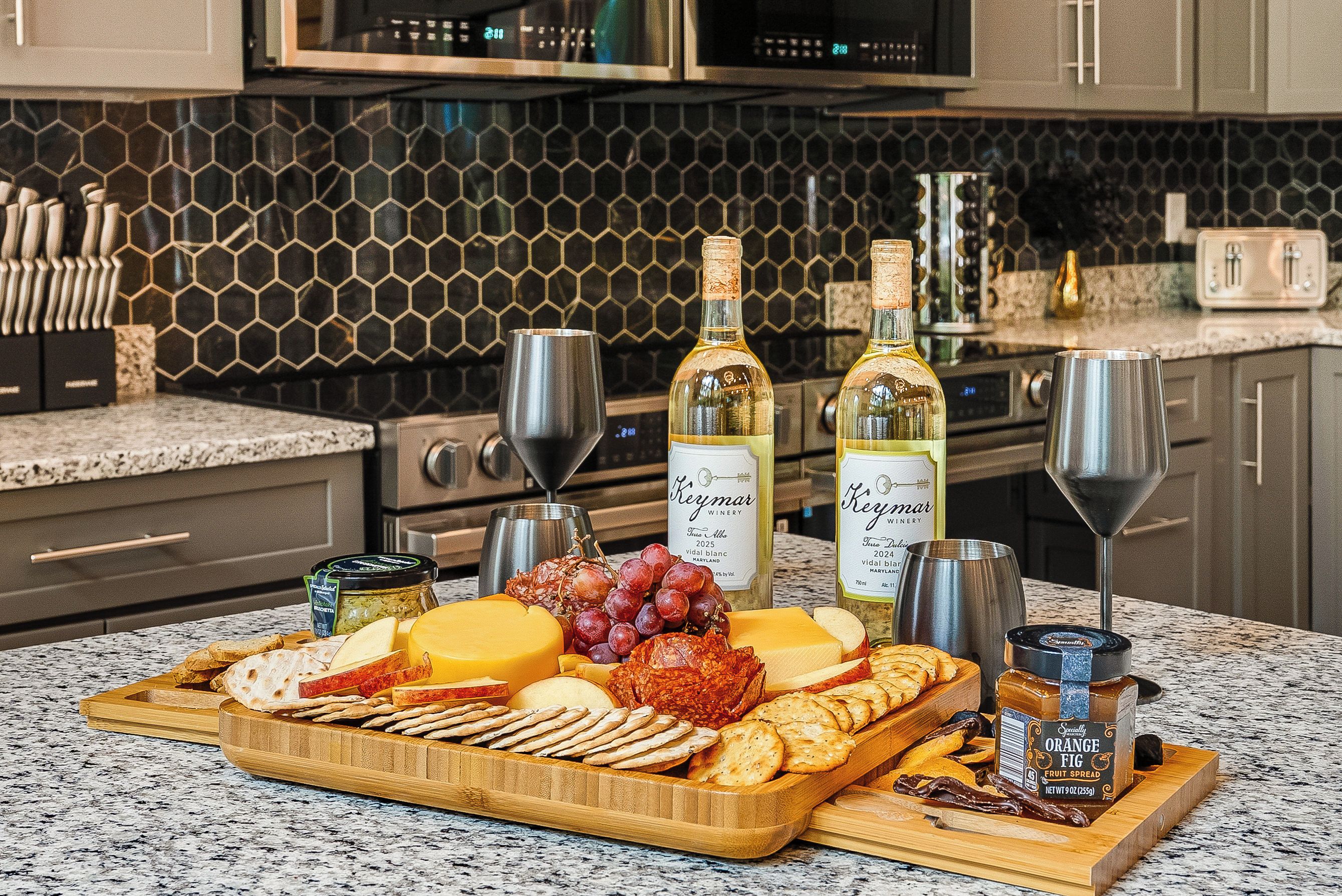 A kitchen counter with a charcuterie board, wine bottles, and a fruit spread.